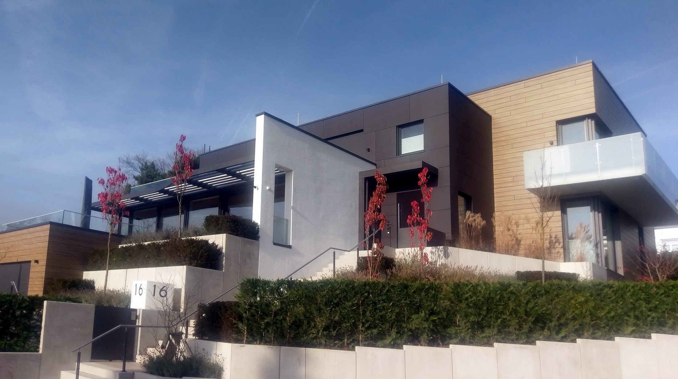 Wohnhaus mit Holz- und Plattenfassade, gestaffelten Terrassen und Gartenmauern